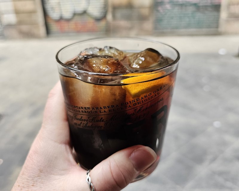 A Glass of Vermut, a dark brown fortified wine served on ice with a slice of orange