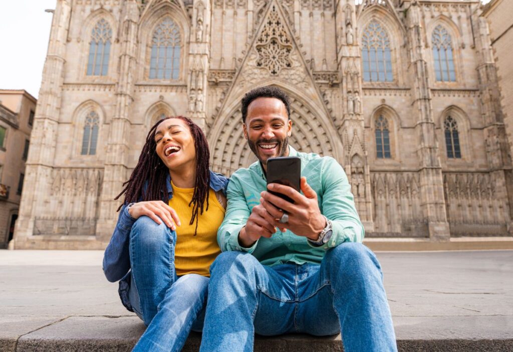 A Couple sitting on the steps of the Cathedral in the Gothic Quarter Barcelona with a Phone in Hand - best eSIM Barcelona