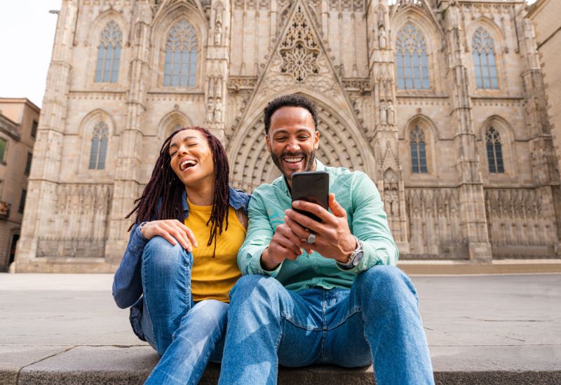 A Couple sitting on the steps of the Cathedral in the Gothic Quarter Barcelona with a Phone in Hand - best eSIM Barcelona