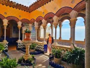 Claire admiring the Colourful Courtyard at the Palau de Maricel Museum in Sitges with yellow arched walkways, tiled walls and a sea view
