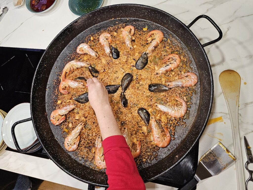 Paella Cooking Classes in Barcelona - Hand reaching over a pan of paella cooking